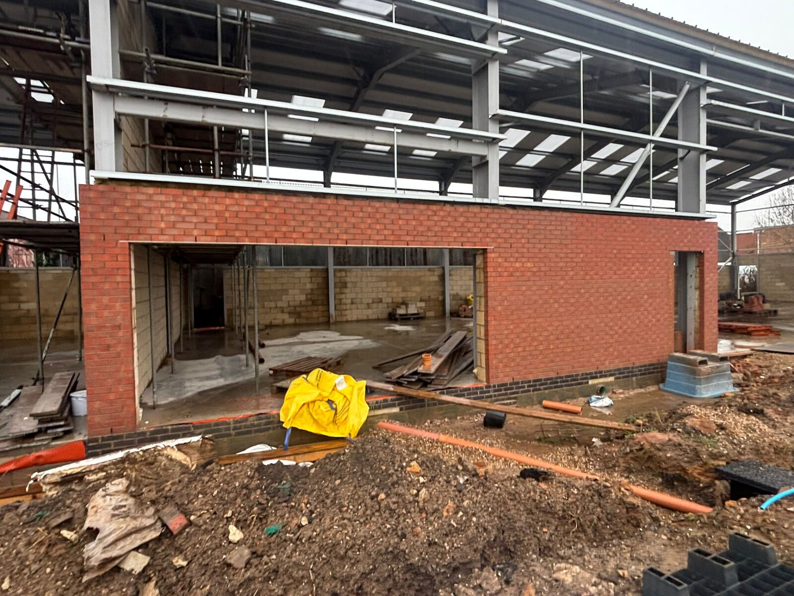 Commercial unit facade in red facing brickwork with blue brick plinth and steel frame behind