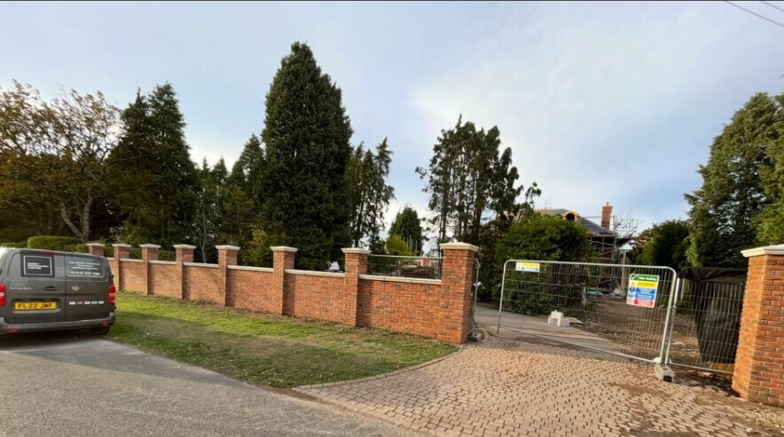 Long red brick boundary wall with evenly spaced piers and cast stone coping in Bramcote