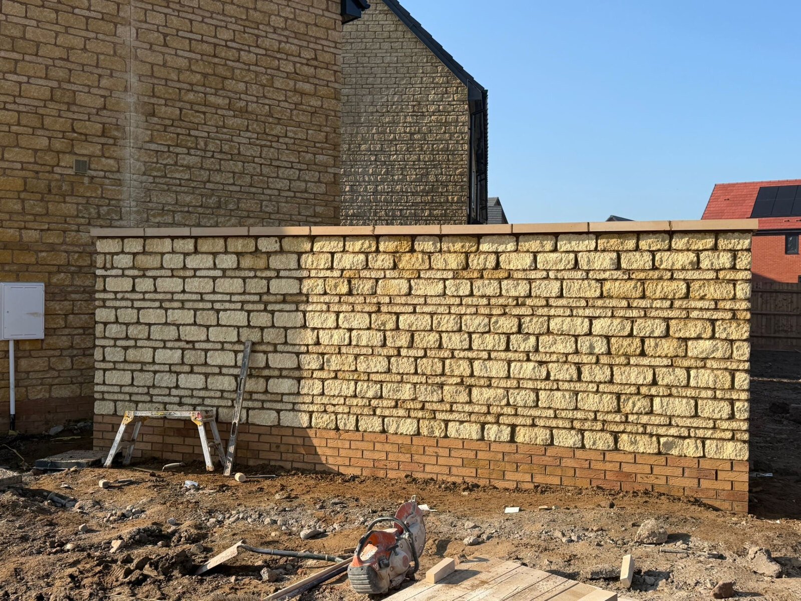 Completed stone boundary wall with brick plinth and coping between new build plots