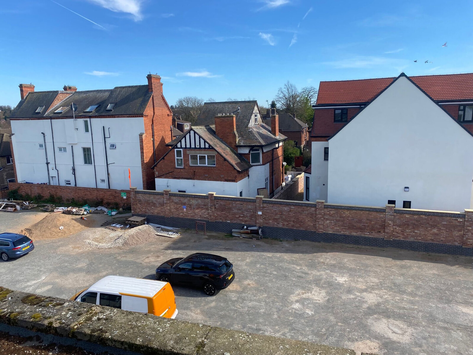 Long red brick boundary wall with blue brick plinth and piers on a development