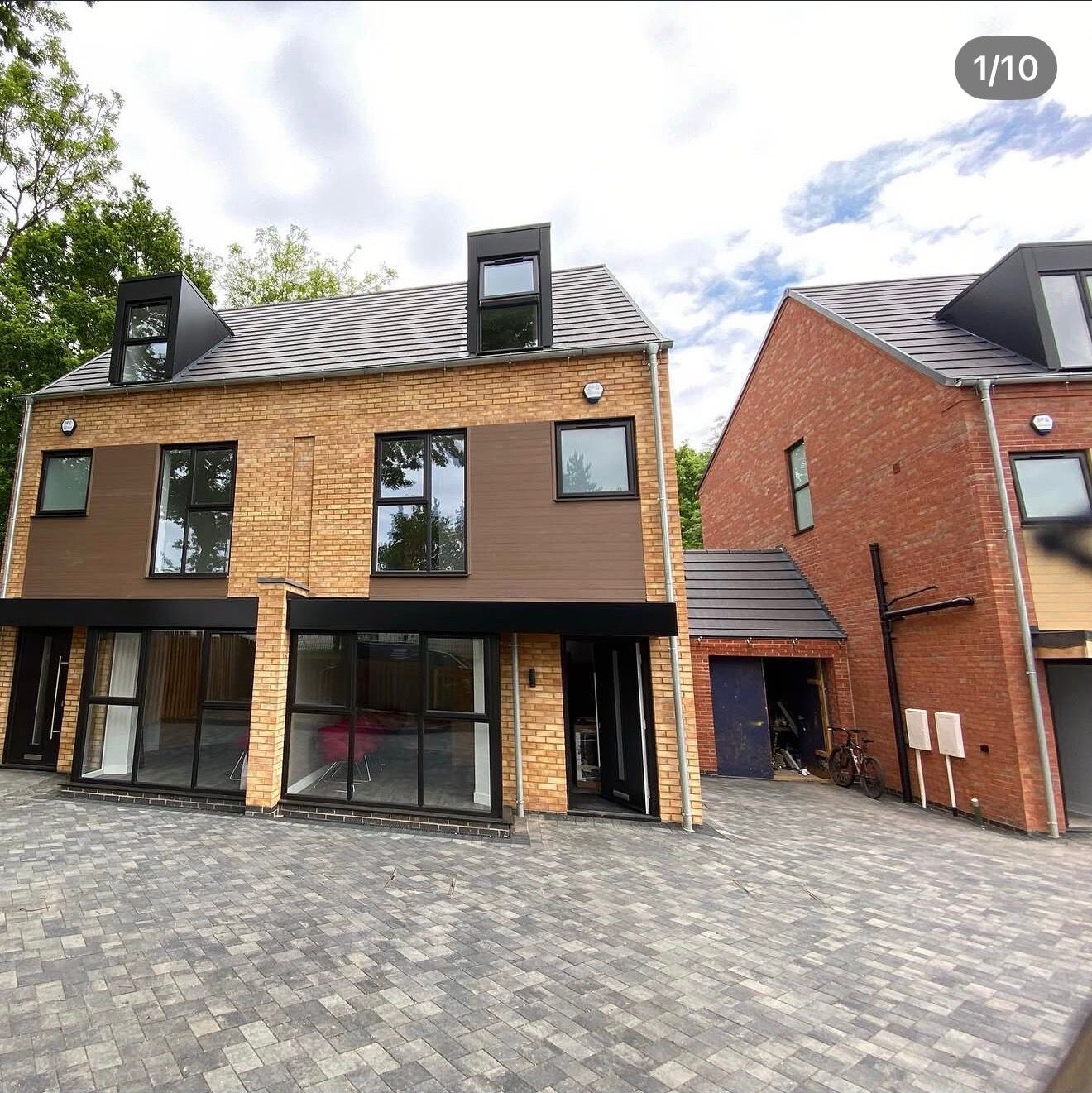 Pair of completed buff brick new build townhouses with dormer windows and block paved frontage