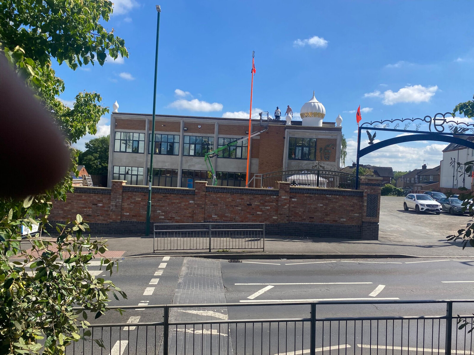 Long brick boundary wall with piers and blue brick plinth outside a Gurdwara