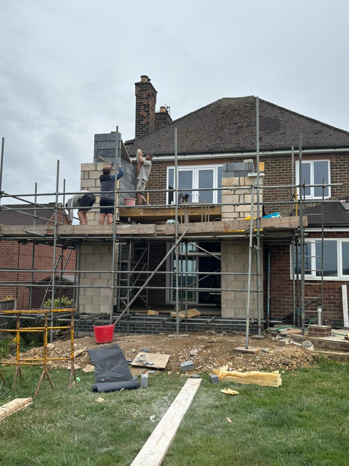 Bricklayers building a two storey rear extension in block and brickwork with scaffolding