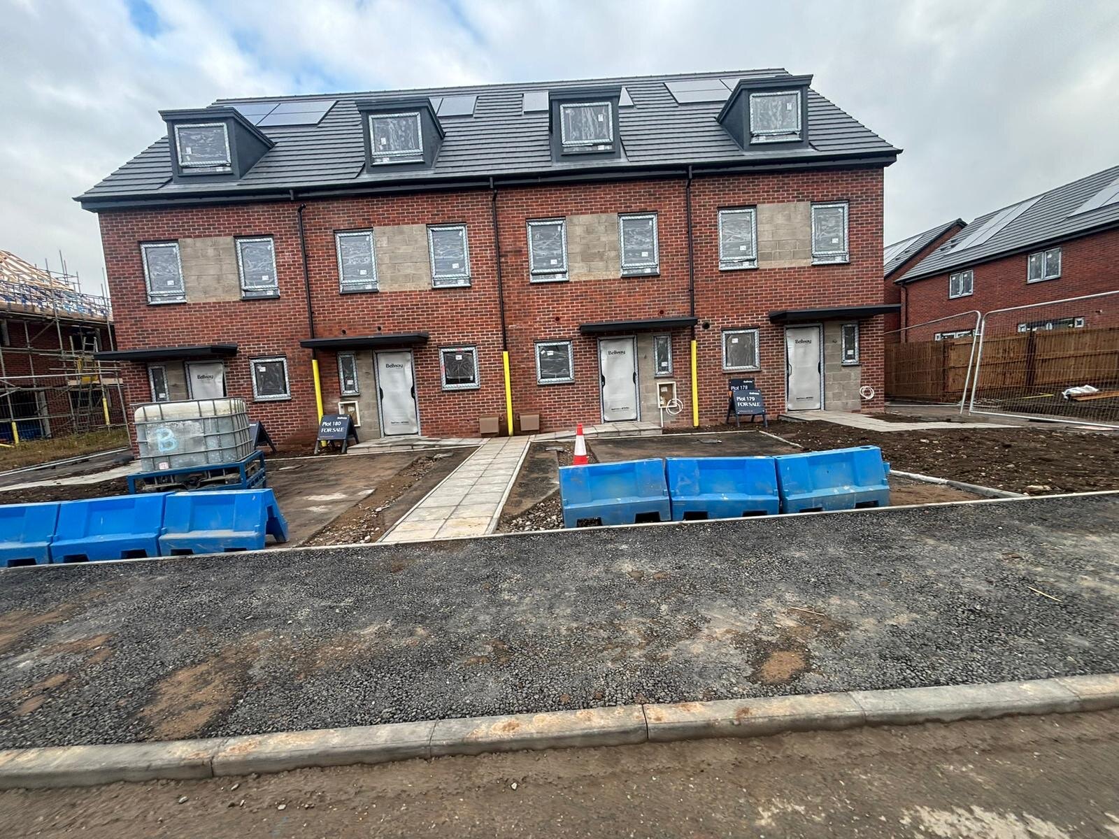 Terrace of new build three storey townhouses with red brick and stone panel elevations under construction